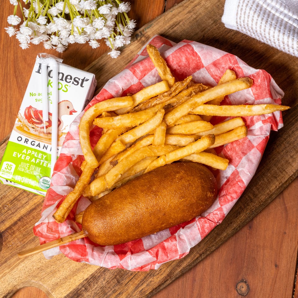 Kids' meal with a corn dog, french fries in a red checkered basket, and an Honest Kids juice box.