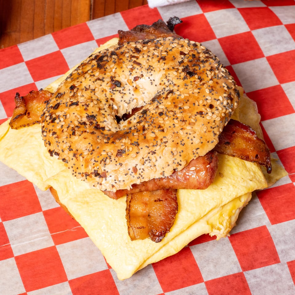Everything bagel with bacon, egg, and cheese on red and white checkered paper.