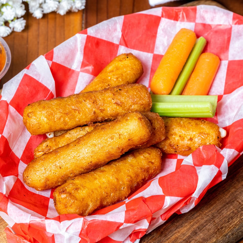 Golden-fried mozzarella sticks and fresh carrot and celery sticks in a red and white checkered basket.