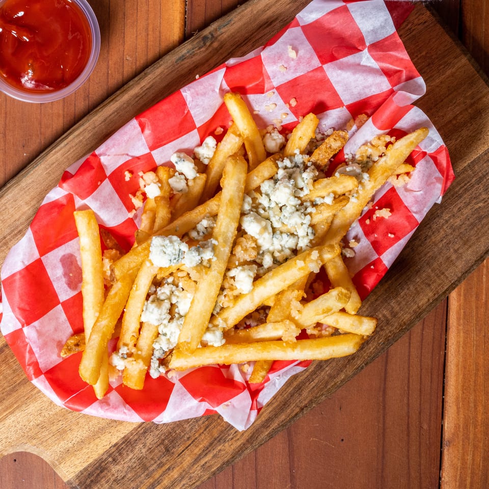 Golden french fries topped with crumbled blue cheese in a red and white checkered paper-lined basket.