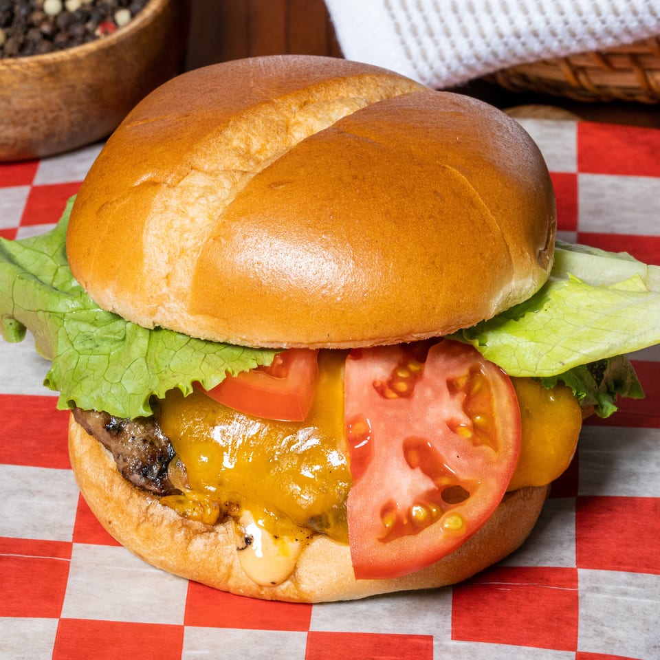Cheeseburger with lettuce, tomato, and melted cheese on a bun, on red and white checkered paper.