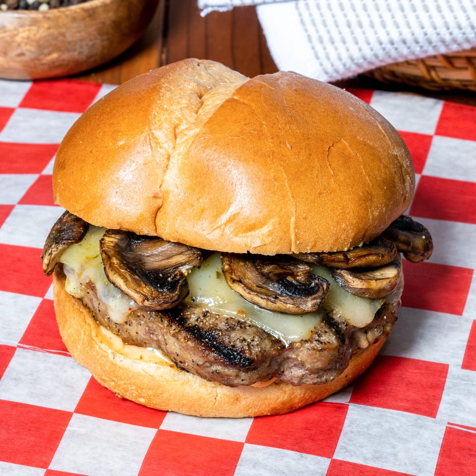 Mushroom Swiss burger on a toasted bun, served on red and white checkered paper.