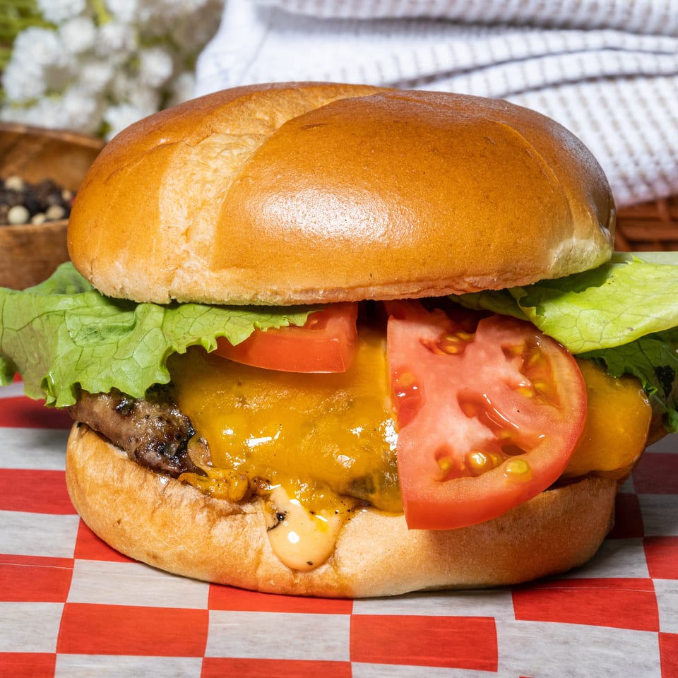 A cheeseburger with lettuce and tomato on a toasted bun, served on red and white checkered paper.